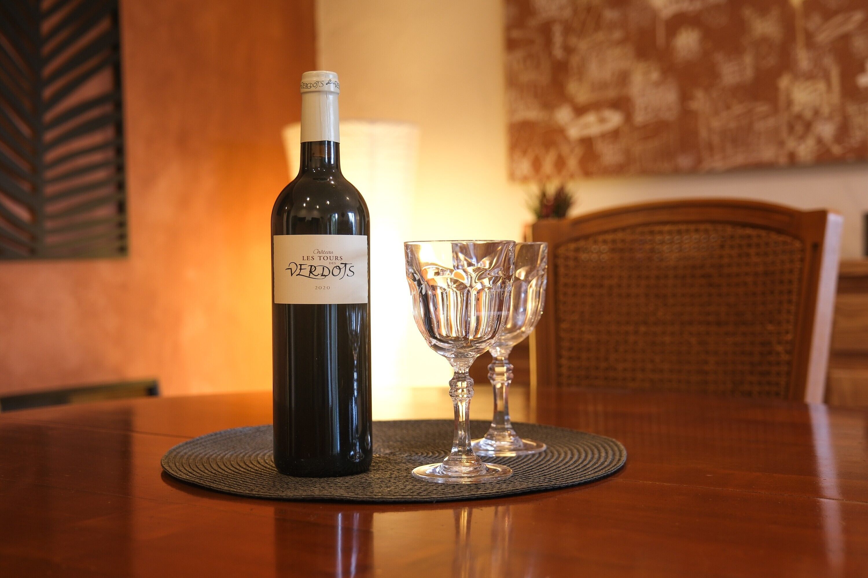 A bottle of wine and two glasses on a table with a placemat.