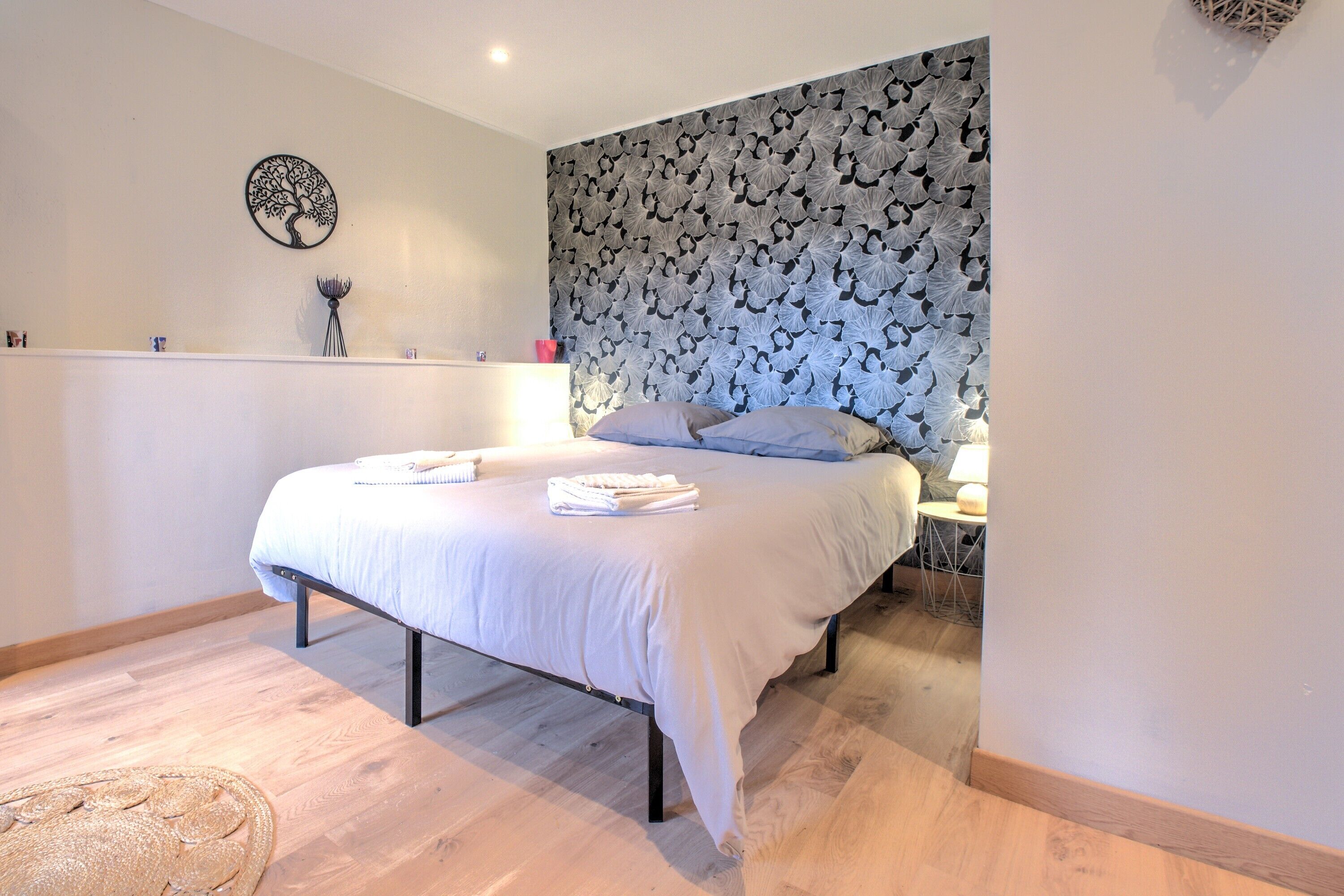 Een slaapkamer met een bed, een kunstwerk aan de muur, een nachtkastje en een lamp.