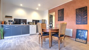 A modern kitchen with grey cabinets, a dining area with a wooden table and chairs, and a wall with decorative leaf patterns.