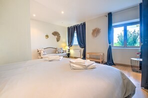 Une chambre avec un grand lit, une table de chevet, une chaise, une fenêtre avec des rideaux et une vue sur la verdure à l’extérieur.