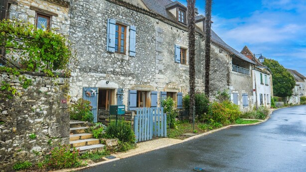 A stone building with blue shutters, a wooden door, and a small garden.