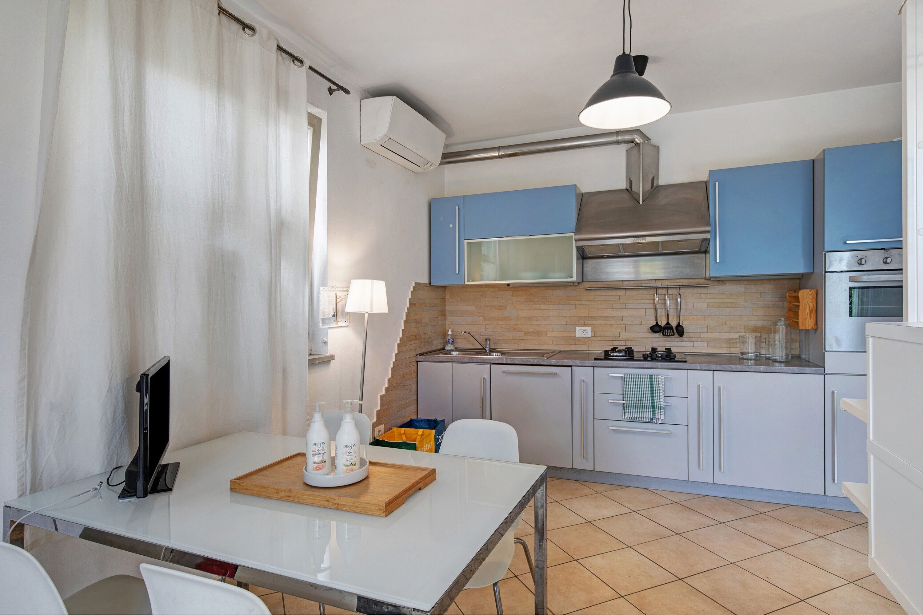 A modern kitchen with blue cabinets, a stainless steel range hood, a microwave, and an oven.
