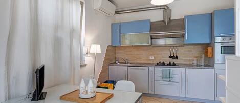 A modern kitchen with blue cabinets, a stainless steel range hood, a microwave, and an oven.
