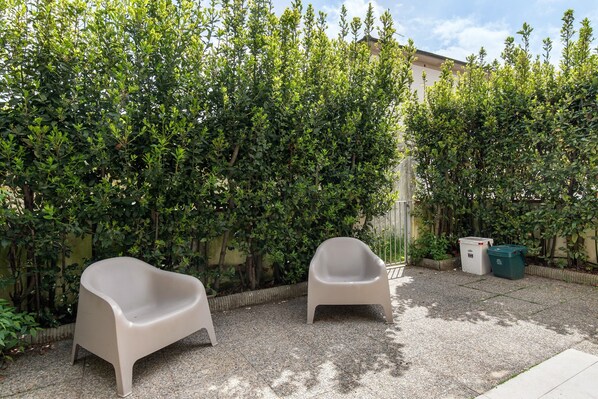 A patio area with two beige plastic chairs, a gravel surface, and a dense green hedge.