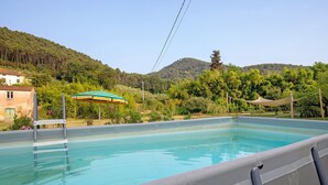 Une piscine dotée d’une terrasse en bois, entourée d’une végétation luxuriante et de collines.