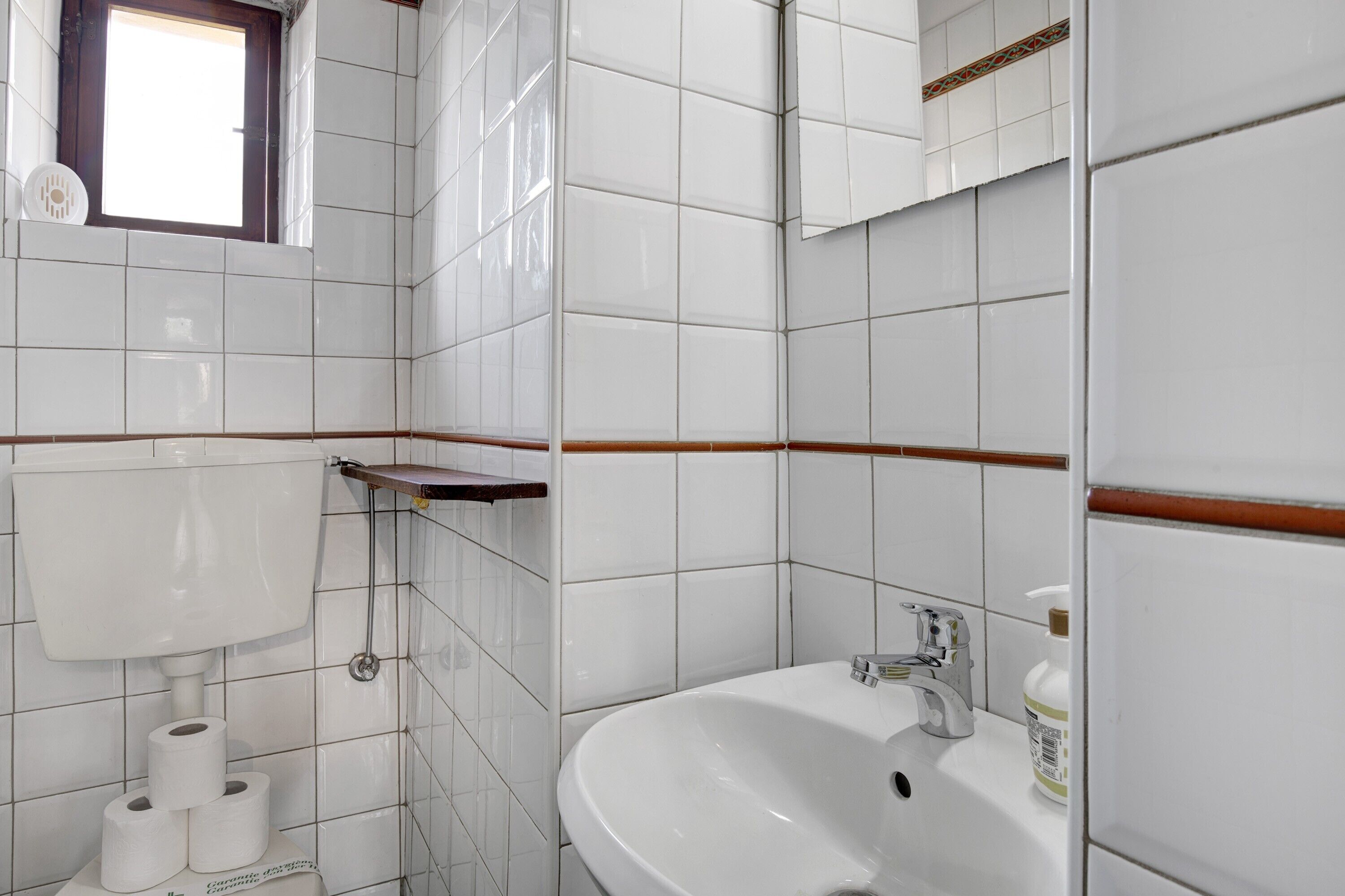 A bathroom with white tiles, a toilet, a sink, and a window.