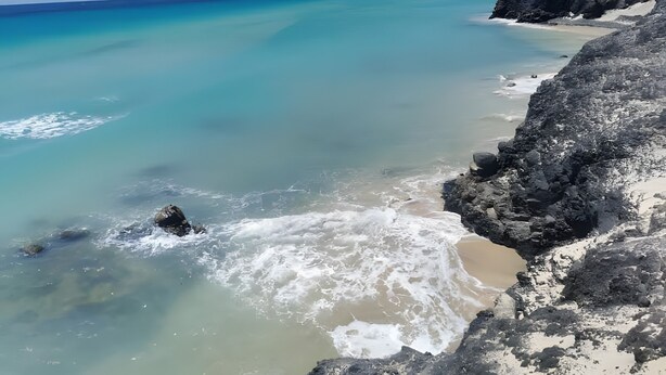 A coastal landscape with clear turquoise waters, rocky cliffs, and a distant mountain. - Vacation Home 'Casa Alisios' with Mountain View, Private Terrace and Wi-Fi (Costa Calma)