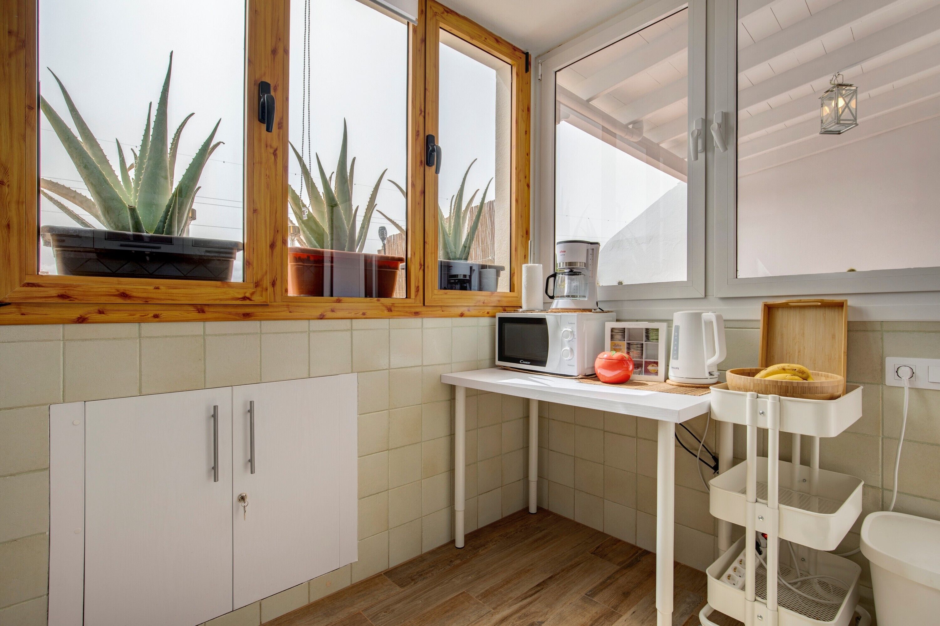 A kitchen with wooden cabinets, a white countertop, a microwave, a coffee maker, and potted plants.