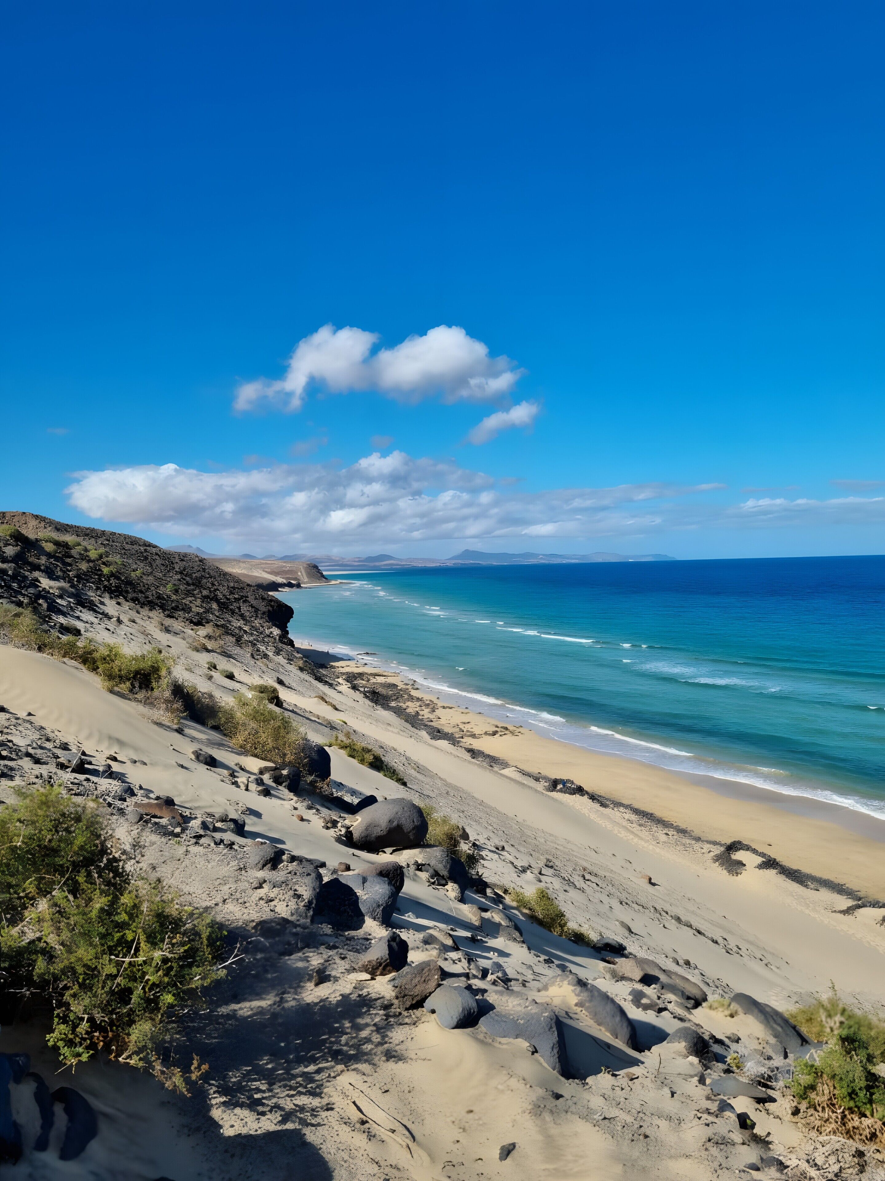 Un paysage côtier avec une plage de sable, un terrain rocheux et un ciel bleu dégagé.