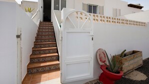 A staircase with patterned tiles leading to a white door, a potted plant, and a wooden crate. - Vacation Home 'Casa Alisios' with Mountain View, Private Terrace and Wi-Fi (Costa Calma)