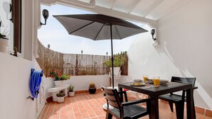 A patio with a table, chairs, a large umbrella, potted plants, and a white wall. - Vacation Home 'Casa Alisios' with Mountain View, Private Terrace and Wi-Fi (Costa Calma)