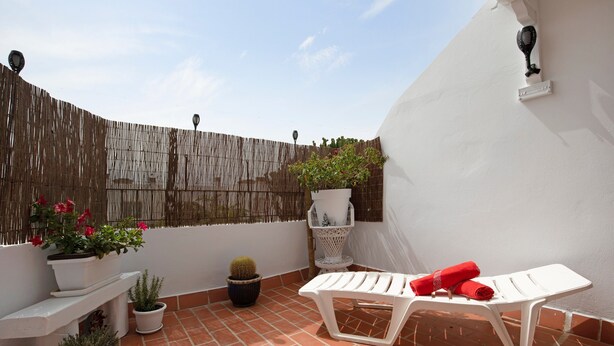 Une terrasse avec une chaise blanche, des plantes en pot et un mur blanc.