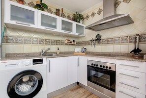 A compact kitchen with a washing machine, oven, and white cabinets.