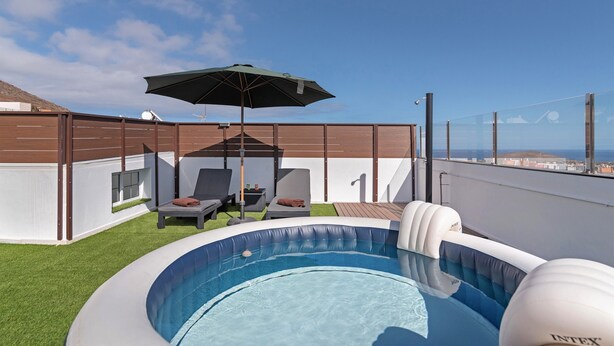 Una piscina en la azotea con jacuzzi, sillas de descanso y una sombrilla.