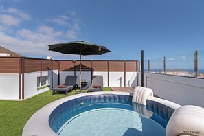 Une piscine sur le toit, avec un jacuzzi, des chaises longues et un parasol.