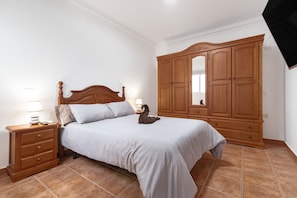 A bedroom with a bed, wooden wardrobe, nightstand, and a wall-mounted TV. - Vacation Apartment 'Unidad B' with Sea View, Wi-Fi and Air Conditioning (Montaña los Velez - Aguimes)