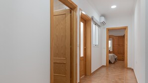 Un pasillo con puertas de madera, suelo de baldosas y un equipo de aire acondicionado en la pared.