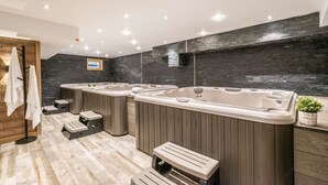 Un baño moderno con tres tinas de hidromasaje, piso de madera y pared de piedra negra.