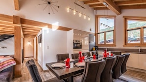 Un comedor moderno con techo de madera, una mesa grande dispuesta para seis personas, y una cocina al fondo.