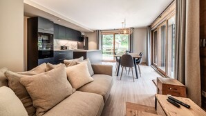 Una sala de estar moderna con un sofá, un comedor con mesa y sillas, y una cocina con gabinetes y electrodomésticos oscuros.