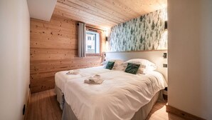 Un dormitorio con techo de madera, cama con ropa blanca, almohadas verdes y una ventana con cortinas.