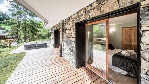 Un dormitorio moderno con fachada de piedra, terraza de madera y vista a un paisaje verde.