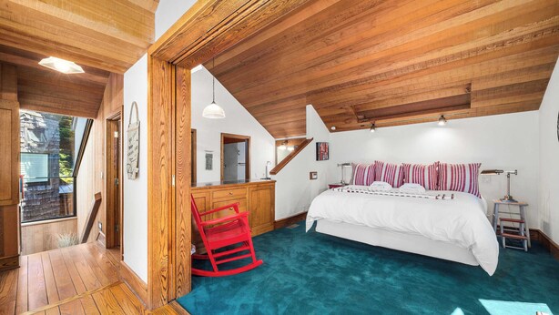 Un dormitorio con techo de madera, una cama con ropa de cama a rayas, una silla roja y un escritorio con espejo.