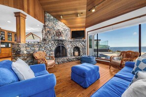 Un intérieur chaleureux avec une cheminée en pierre, un plafond en bois et une vue sur l’océan.