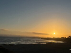 Une scène de plage avec un coucher de soleil, l’océan et une côte lointaine.
