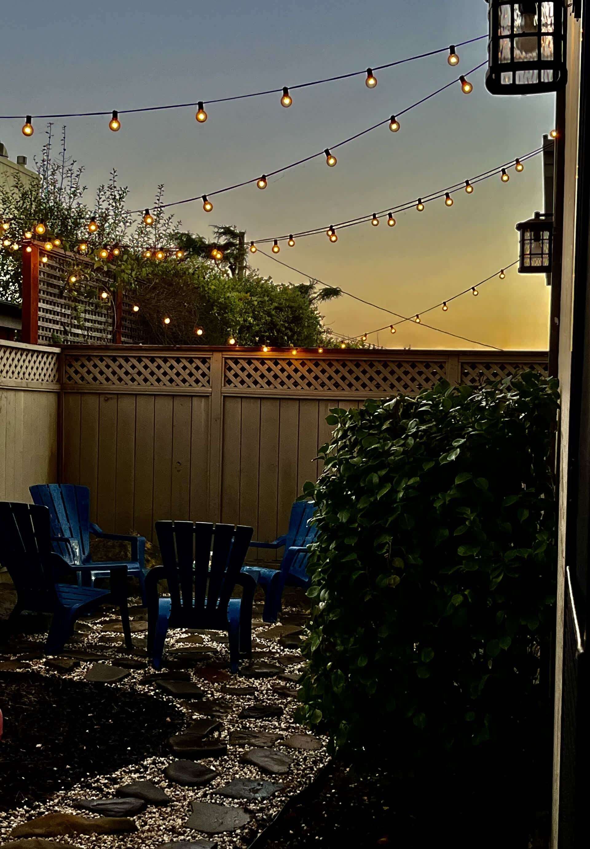 Un espace patio agrémenté de guirlandes lumineuses, de chaises bleues et d’une clôture en bois.