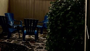 Un patio con luces colgantes, sillas azules y una valla de madera.