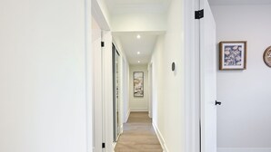 Un passadís amb parets blanques, un sòl de marbre i una porta de fusta al final.