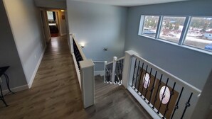 A staircase with wooden flooring and white railings, leading to a landing with a view of a snowy landscape through a window. - Spacious 6-bedroom+ Studio Apartment with 12+ Guests-Dog friendly in Homer Hills (Homer)