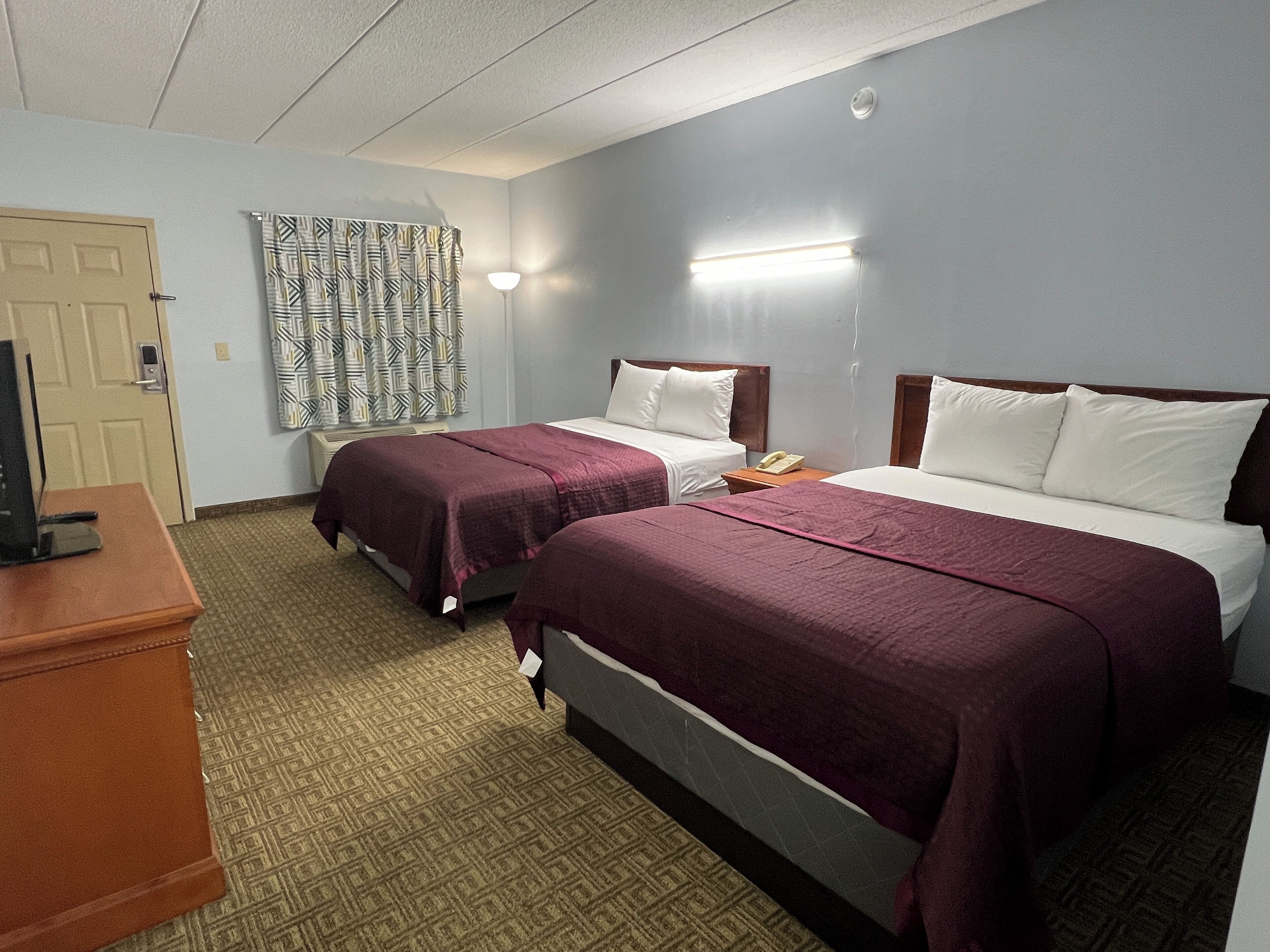 A hotel room with two beds, a desk, a telephone, and a patterned curtain.