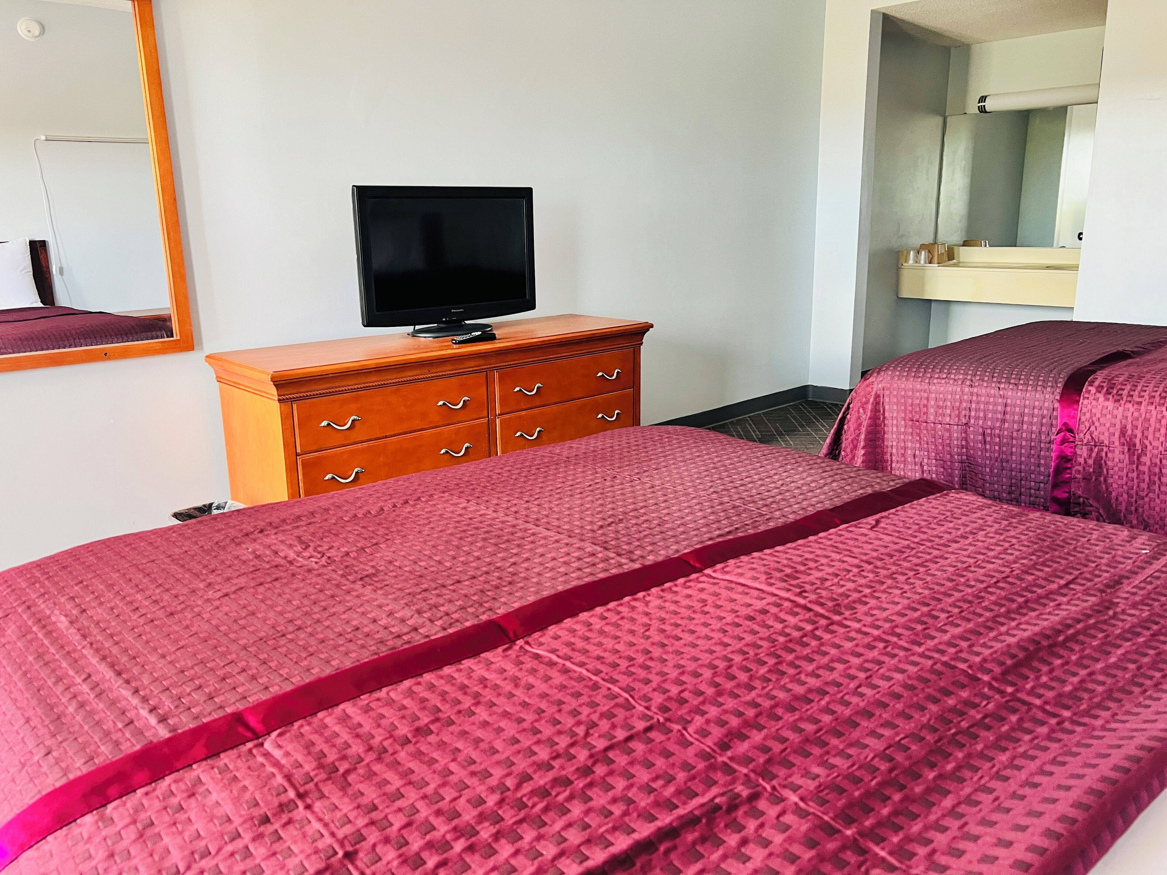 Habitación de hotel con una cama, un aparador de madera, un televisor y un espejo.