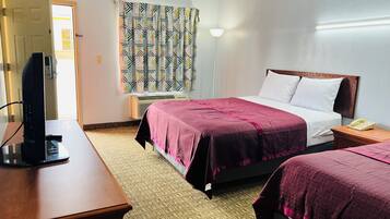 A hotel room with a bed, bedside table, TV, and a window with patterned curtains.