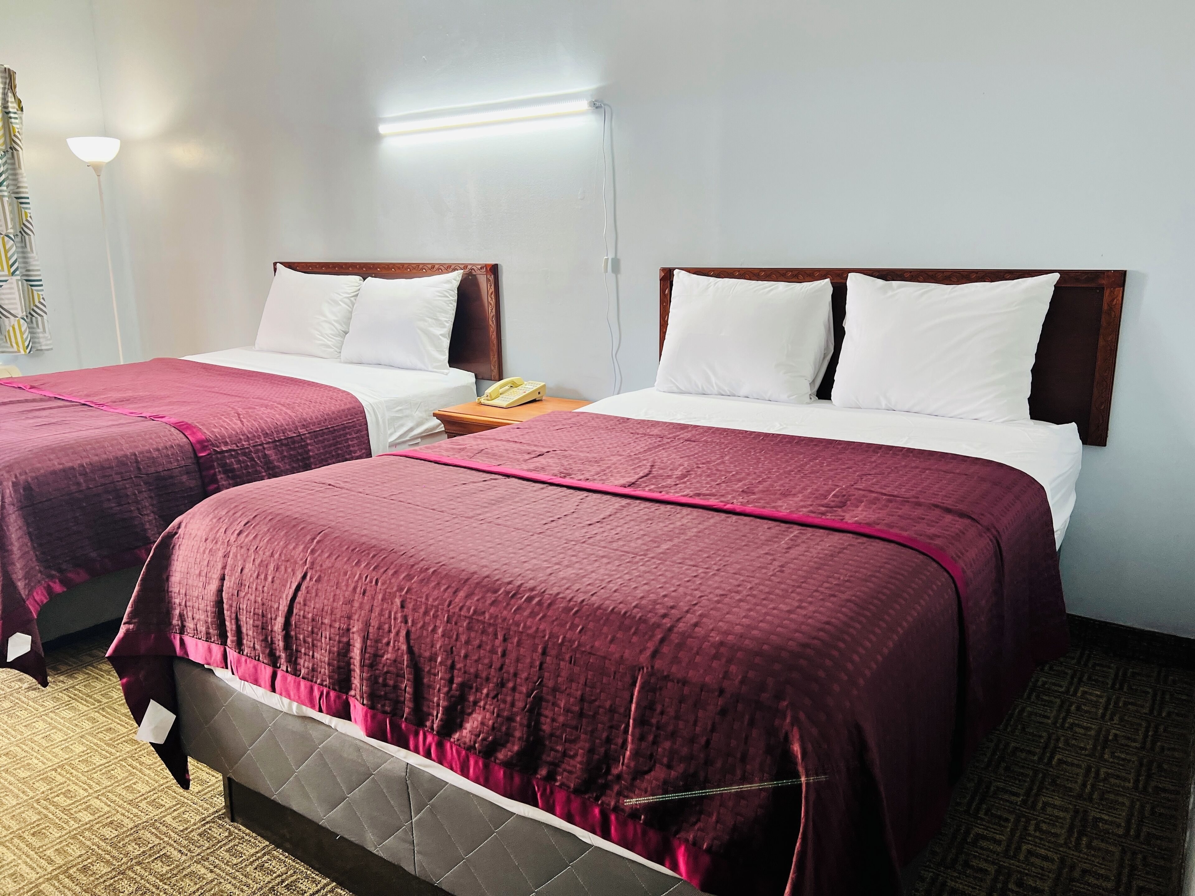A hotel room with two beds, each with a wooden headboard and white bedding. There is a bedside table with a telephone on it.