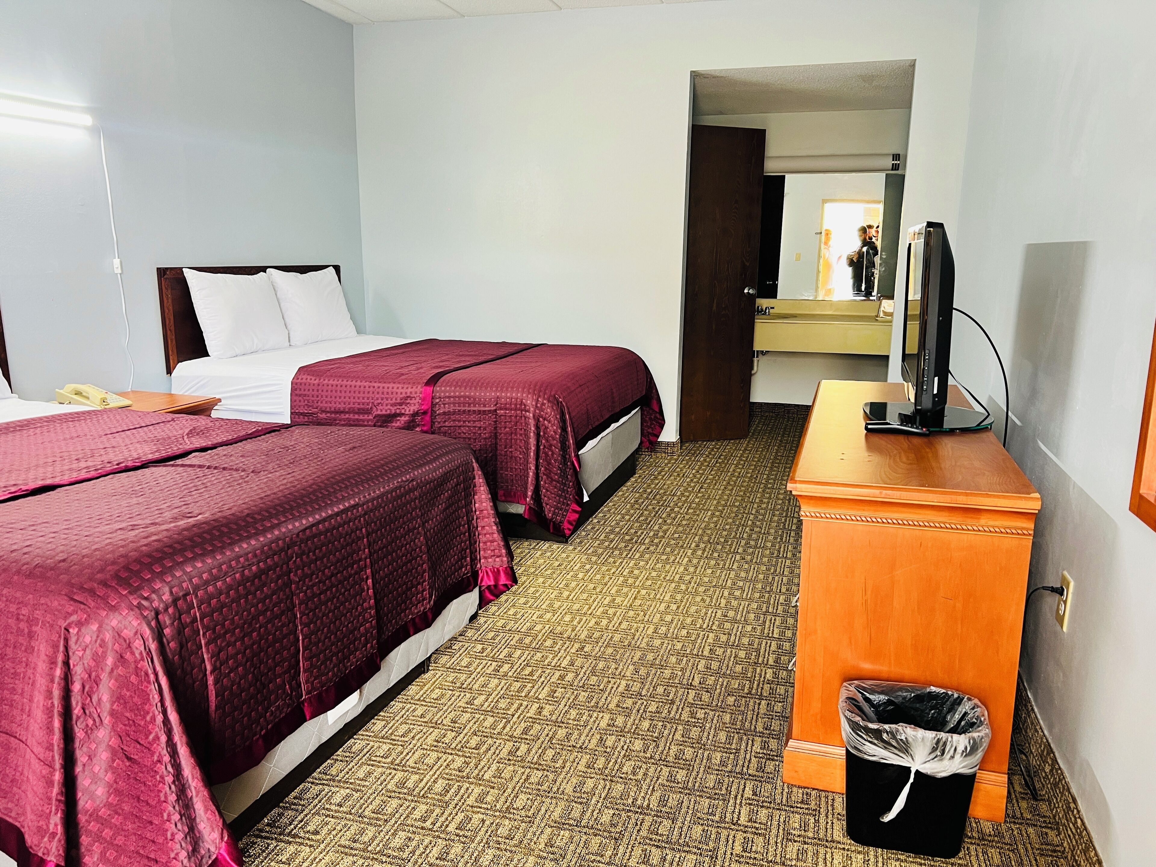 A hotel room with two beds, a wooden desk, a trash bin, and a television.