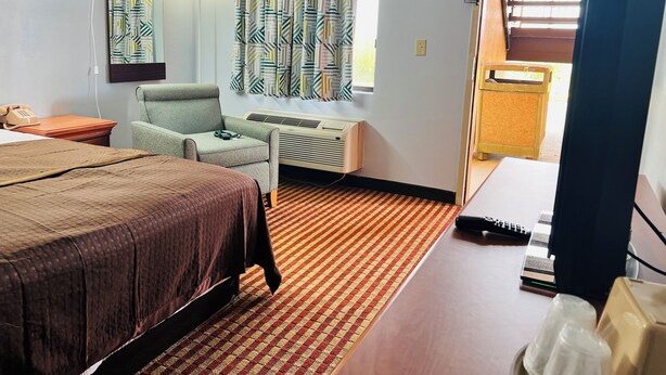 Une chambre d’hôtel comprenant un lit, un bureau, une chaise, une lampe de bureau, une fenêtre avec des rideaux, un climatiseur et une vue sur l’extérieur.