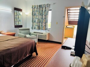 Hotelkamer met een bed, bureau, stoel, bureaulamp, raam met gordijnen, airconditioning en uitzicht op buiten.