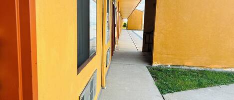 A corridor with yellow walls and large windows, leading to a building entrance.