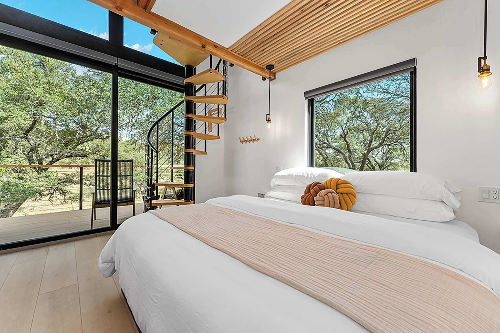Un dormitorio con una cama grande, una escalera de madera y vistas a árboles a través de amplios ventanales.