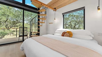 Un dormitorio con una cama grande, una escalera de madera y vistas a árboles a través de amplios ventanales.
