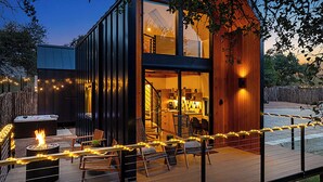 Una cabaña moderna con terraza, mobiliario exterior y un brasero.