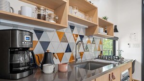 Una cocina moderna con cafetera, hervidor y estantes con vajilla y cristalería.