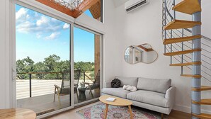 A modern living room with a sofa, a coffee table, and a spiral staircase. - The Live Oak at Meridian, Hot tub & Firepit! (Fredericksburg)