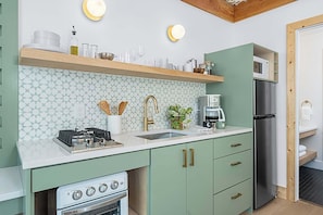 Une cuisine compacte équipée d’une cuisinière à gaz, d’un four et d’un micro-ondes, le tout installé sur une étagère intégrée.