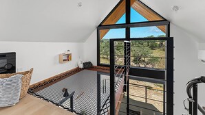 Ein Zimmer mit hohen Decken, einem großen Fenster und Blick ins Freie.