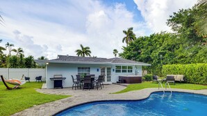 Un patio trasero con piscina, zona de barbacoa y mobiliario exterior.