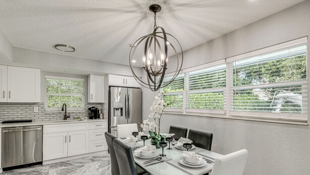 Una cocina moderna con armarios blancos, un lavavajillas de acero inoxidable y un comedor con una mesa blanca dispuesta para cuatro.
